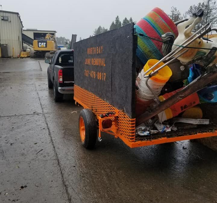 Grey and orange trailer attached to van carrying junk