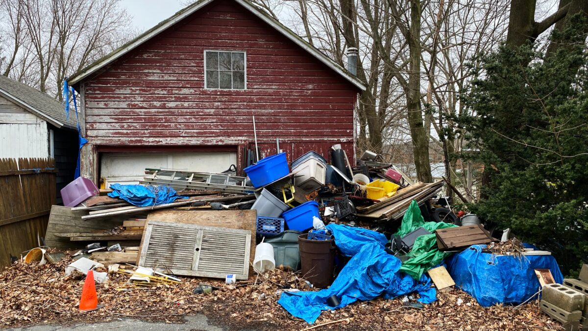 Brown house with piles of trash and garbage in the front yard